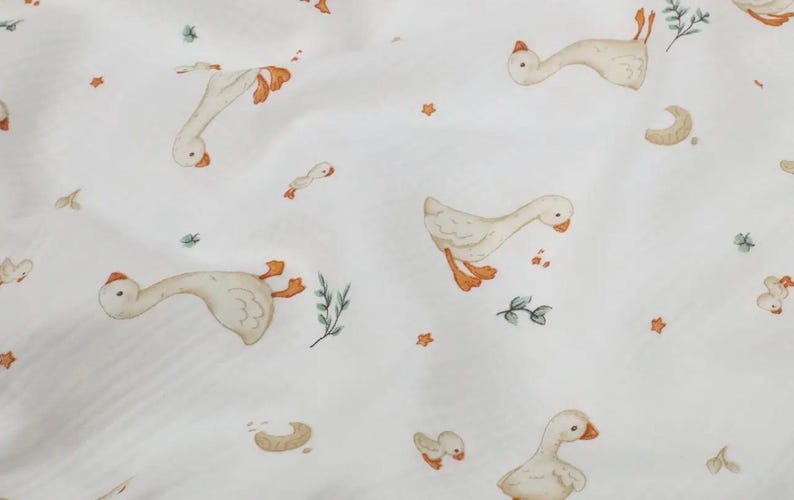 May include: White fabric with a repeating pattern of watercolor geese in various poses. The geese have orange beaks and feet. Scattered among the geese are small orange stars, green sprigs, and crescent shapes.
