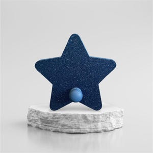May include: A navy blue star-shaped wall hook with a glittery finish and a small blue knob. The hook is mounted on a white, layered, stone-like base, creating a decorative and functional item.