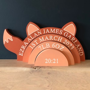 Puede incluir: Un anuncio de nacimiento de madera en forma de zorro con el texto "Ezra Alan James Garland", "1 de marzo de 2023", "7lb 6oz" y "20:21".