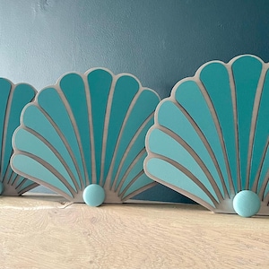 Peut inclure: Trois décorations murales en forme de coquille de couleur bleu sarcelle et gris avec un accent nacré au bas de chacune.