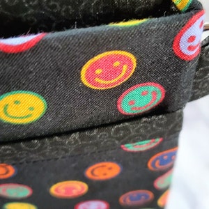 May include: Black fabric pouch with a zipper closure. The fabric is patterned with colorful smiley faces.