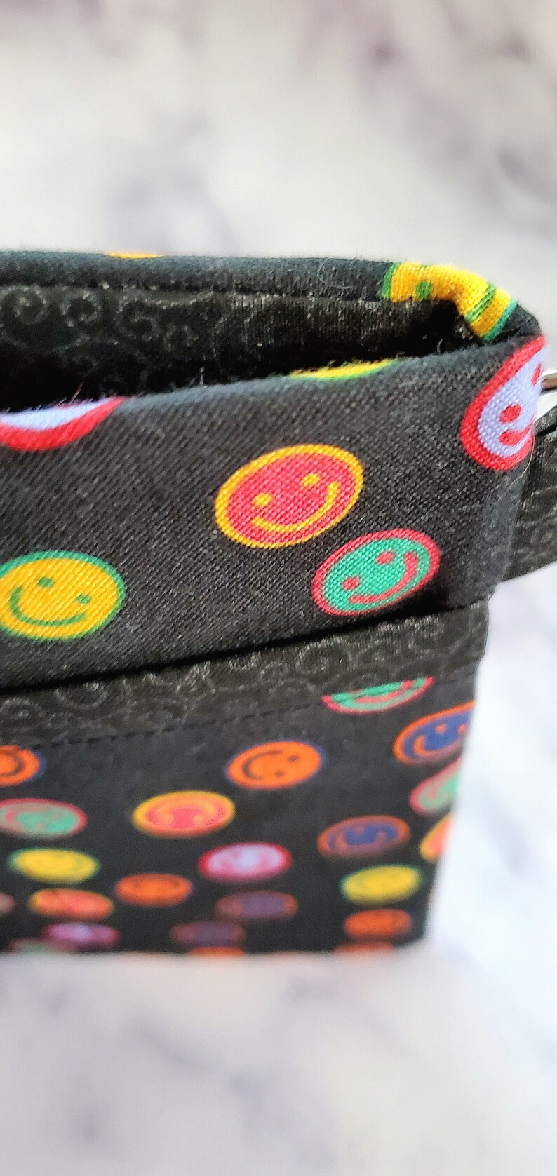 May include: Black fabric pouch with a zipper closure. The fabric is patterned with colorful smiley faces.