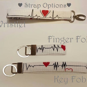 May include: Three white fabric keychains with a black EKG line and red heart designs. The keychains are labeled "Wristlet", "Finger Fob", and "Key Fob".