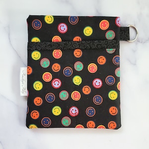 May include: Black fabric pouch with a colorful smiley face pattern. The pouch has a zipper closure and a metal ring attached to the top. The pouch is labeled "Amethyst Alley".