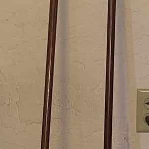 May include: Two antique wooden walking canes. One cane has a rounded top and the other has a brass top. Both canes are dark brown with brass accents at the bottom.