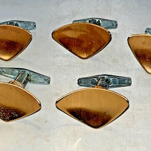 May include: Five pairs of vintage cufflinks with a copper-colored, diamond-shaped face. The cufflinks have a silver-colored, hinged backing. The copper faces have a brushed metal finish and are slightly curved.
