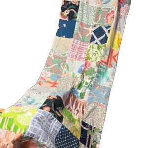 May include: A patchwork quilt featuring a variety of fabric squares in diverse colors and patterns, including floral prints, plaid, checkered designs, and solid blocks. The textile is constructed from multiple stitched segments of cotton fabric.