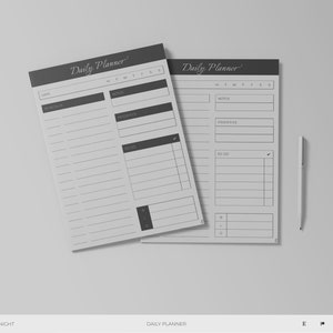 Op de afbeelding: Twee zwart-witte dagelijkse plannerpagina's met de tekst "Daily Planner" bovenaan. De pagina's zijn gestreept en hebben secties voor notities, prioriteiten en takenlijsten. Een witte pen ligt op een grijs oppervlak naast de pagina's.