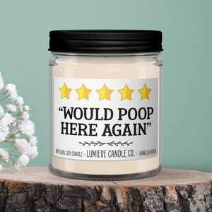 May include: A clear glass jar candle with a black lid, sitting on a wooden slice. The candle has a label with the text "WOULD POOP HERE AGAIN" and five gold star ratings. The background is a light teal color with white flowers.