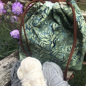 May include: A green drawstring bag with a floral pattern, filled with two balls of yarn, one white and one gray.