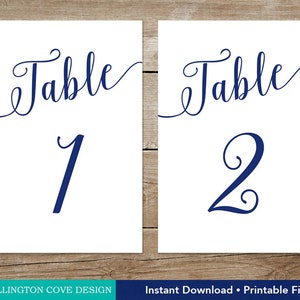 May include: Two white rectangular table number cards. The word "Table" is written in a navy blue script font above the numbers 1 and 2. The text "Wellington Cove Design" and "Instant Download &bull; Printable File" are at the bottom.