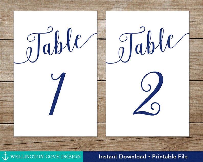May include: Two white rectangular table number cards. The word "Table" is written in a navy blue script font above the numbers 1 and 2. The text "Wellington Cove Design" and "Instant Download &bull; Printable File" are at the bottom.