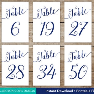 May include: Six white table number cards with navy blue script and numbers. The cards are arranged on a wooden surface. Numbers include 6, 19, 27, 28, 34, and 50. The text "Instant Download &bull; Printable File" is at the bottom.