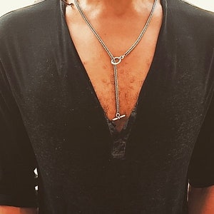 Può includere: Una collana a catena d'argento con un ciondolo a forma di T. La collana è a strati e ha una chiusura ad anello.