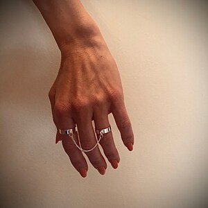 May include: A set of three silver rings connected by a chain. The rings are worn on the index, middle, and ring fingers.