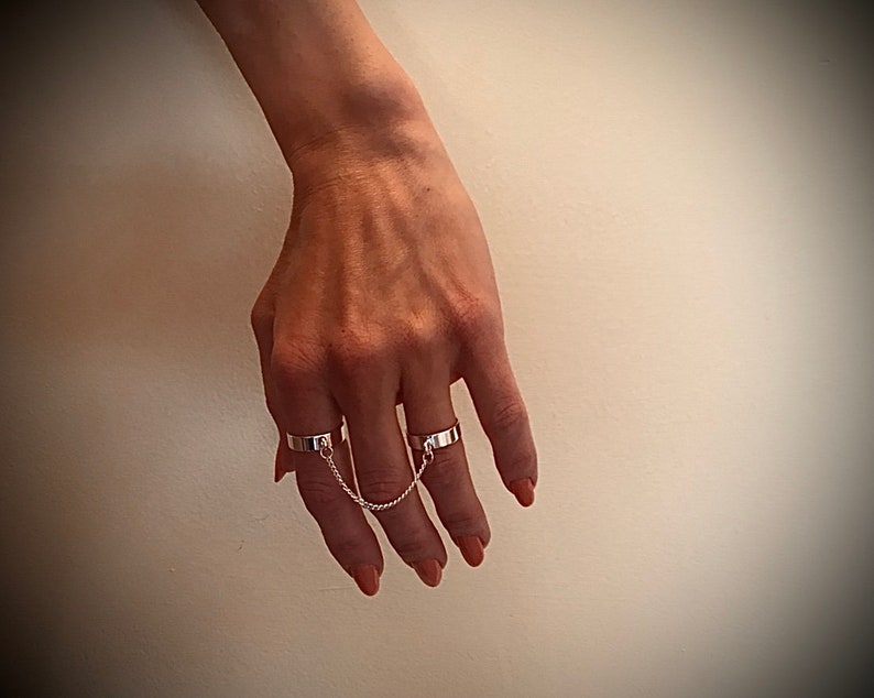 May include: A set of three silver rings connected by a chain. The rings are worn on the index, middle, and ring fingers.