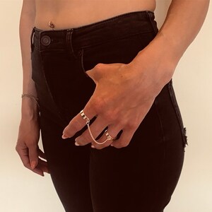 May include: A person wearing black jeans and a gold chain ring on their finger.
