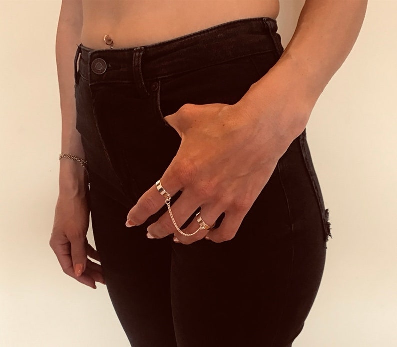 May include: A person wearing black jeans and a gold chain ring on their finger.