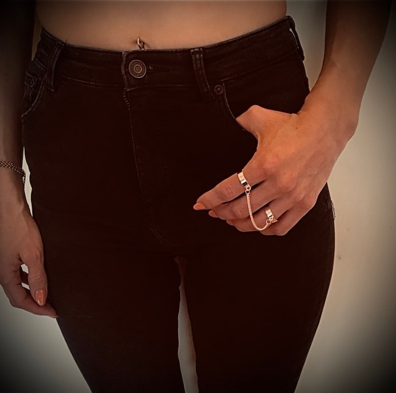 May include: A gold chain ring set with two connected rings. The rings are worn on the index and middle finger.