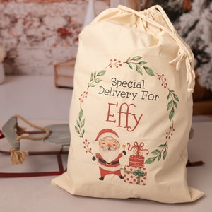 May include: A white canvas Santa sack with a green wreath design and the text "Special Delivery For Effy". A cartoon Santa Claus is holding a bell and a stack of wrapped presents.