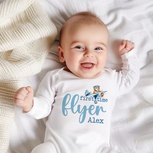 Pu&ograve; includere: Un body bianco per neonato con un grafico di aereo blu e il testo "first time flyer Alex".