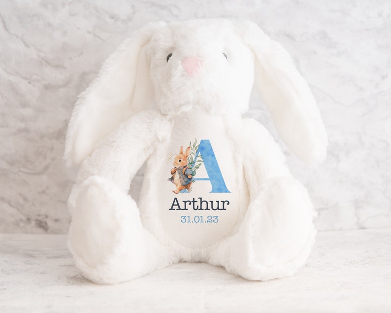 May include: White plush bunny with a blue and watercolor floral letter A and the name Arthur and the date 31.01.23 printed on the chest.