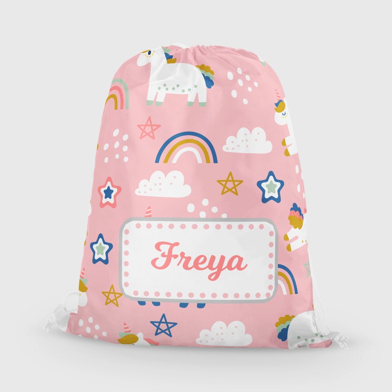 May include: Pink drawstring bag with a unicorn, rainbow, and star pattern. The bag has a white name tag with the name "Freya" printed on it.