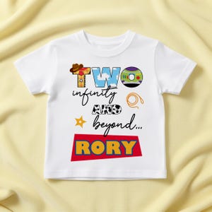 May include: White toddler t-shirt with a colourful graphic design. The design includes the words "TWO infinity AND beyond..." and the name "RORY" in large, bold letters. The shirt features cartoon-style illustrations.