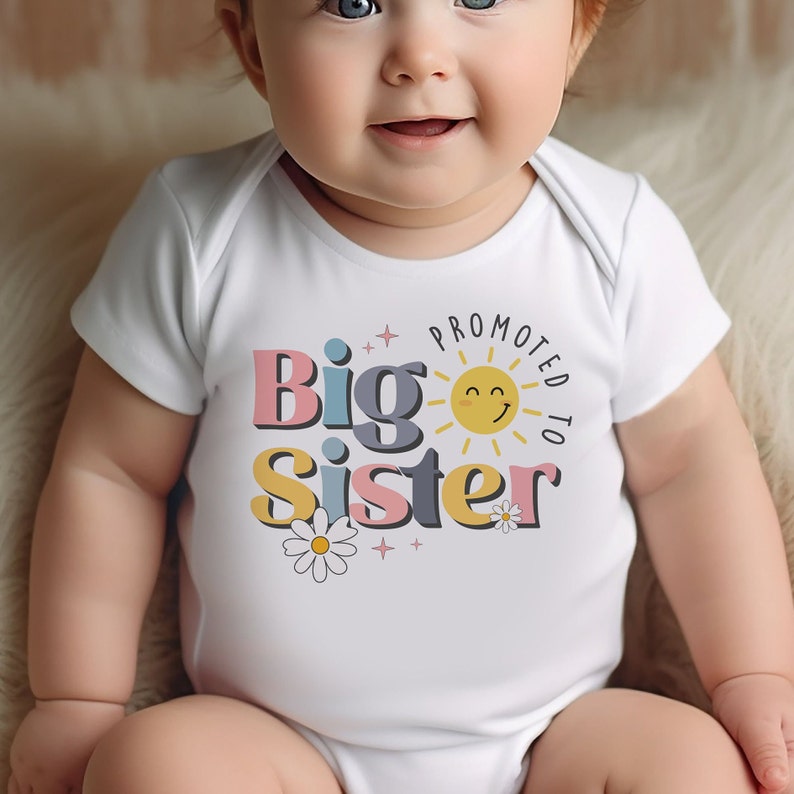 May include: A white baby onesie with the text "Promoted to Big Sister" in colorful letters with a smiling sun and daisies.