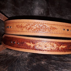 May include: Two brown leather belts with intricate floral tooling and silver studs. The belts are stacked on top of each other.