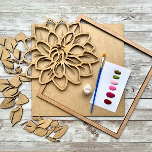 May include: A wooden craft kit featuring a large flower, leaves, and a frame. The kit includes paint colors in shades of green, pink, and red, a paintbrush, and a small bottle of glue. "Glue" is written on the bottle.