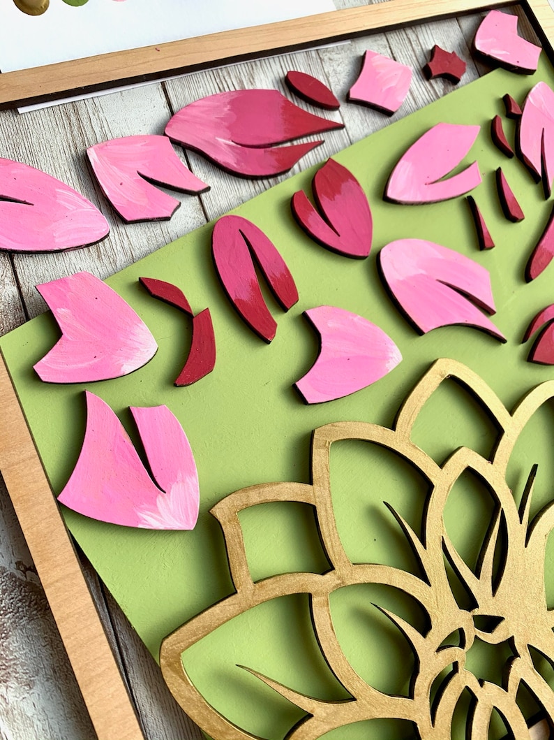 May include: A wooden craft project featuring a large gold mandala with pink and red flower petals surrounding it. The petals are painted and arranged on a green background.