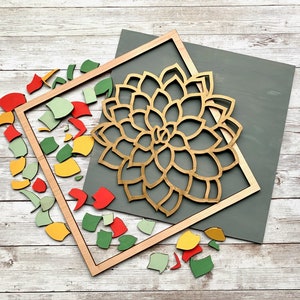 May include: A wooden frame with a gold-colored cutout of a flower design. The frame is surrounded by colorful wooden pieces.