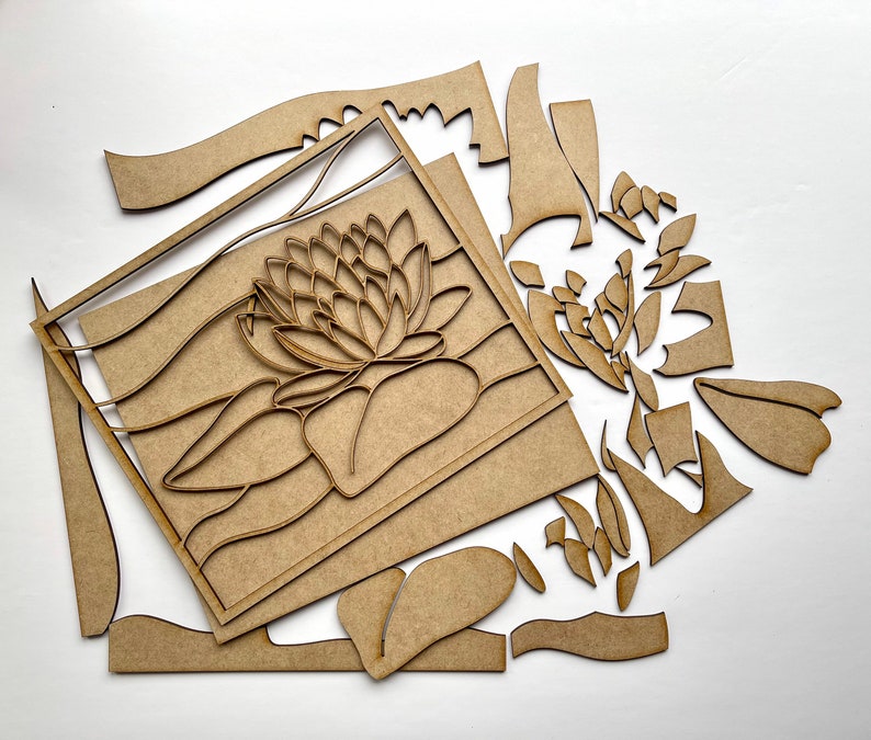 Op de afbeelding: Een houten knutselset met een lotusbloemontwerp. De set bevat meerdere houten onderdelen die kunnen worden geassembleerd om een decoratieve wandhanger of ander knutselproject te maken.