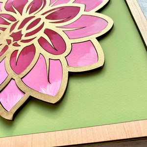 May include: A framed pink and gold flower with a green background. The flower is made of wood and has a 3D effect.