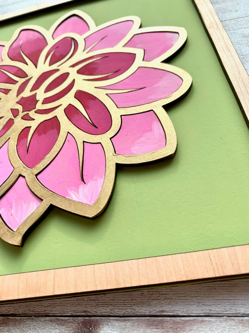 May include: A framed pink and gold flower with a green background. The flower is made of wood and has a 3D effect.