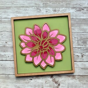 May include: A pink and red wooden flower with layered petals is mounted on a green background in a wooden frame.