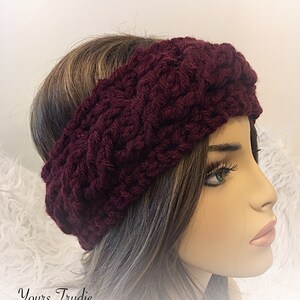 May include: A burgundy knitted headband with a braided pattern. The headband is worn on a mannequin with long brown hair.