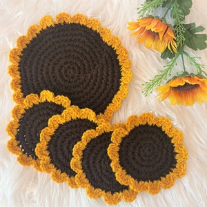 May include: Set of four crocheted sunflower coasters in brown and yellow. The coasters are round and have a scalloped edge.
