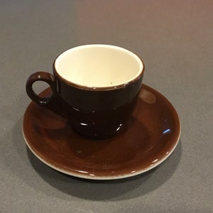 May include: A brown ceramic coffee cup with a white interior and a matching saucer. The cup and saucer are both empty.