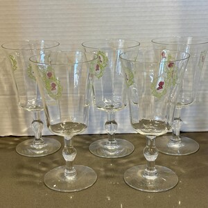 May include: Set of six clear glass wine glasses with a green and pink floral design. The glasses have a tall, slender stem and a round base.