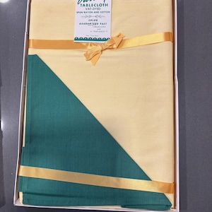 May include: A boxed yellow tablecloth with a green corner accent and gold ribbon. The tablecloth is labeled "Variety" and includes the text "VAT-DYED SPUN RAYON AND COTTON". The box is white.
