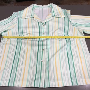 May include: A white, green, and yellow striped button-up shirt with long sleeves. The shirt is measured across the chest with a tape measure, showing a measurement of 19 inches.