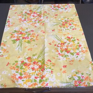 May include: A yellow fabric with a floral pattern featuring bouquets of orange, red, and white flowers. The fabric has a subtle texture and a slightly faded appearance.