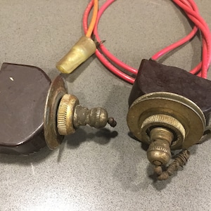 May include: Two vintage brown and brass light pull switches with red and orange wires. The switches have a decorative brass pull chain and a brass knob. The wires are connected to a brown plastic housing.