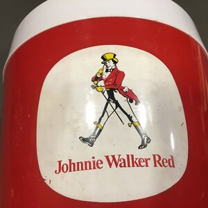 May include: Red and white cooler with a Johnnie Walker Red label featuring a man in a red jacket and black pants walking with a cane. The label also includes the text "Johnnie Walker Red".