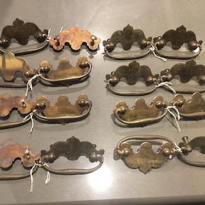 May include: Ten antique brass cabinet drawer pulls with ornate designs. The pulls have a slightly tarnished finish and are in good condition.