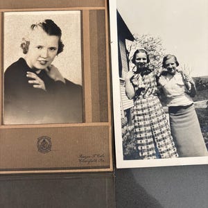May include: Two vintage black and white photographs. One is a portrait of a woman in a dark top, framed in a brown photo album. The other shows two women outdoors, one in a plaid dress. The album has text.