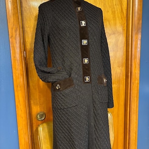 May include: A dark brown, long-sleeved coat with a high collar and a textured knit pattern. The coat features brown suede accents on the front, pockets, and cuffs, with gold-colored square buttons. The coat is knee-length.