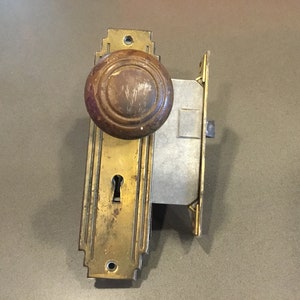 May include: A vintage brass door knob with a wooden handle and a keyhole. The knob is attached to a brass plate with a decorative design.